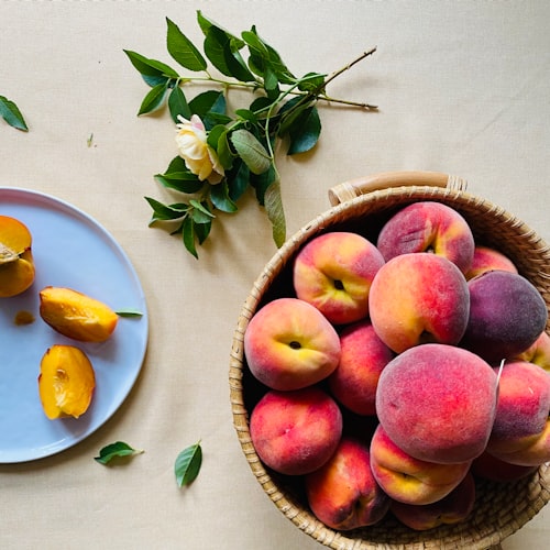 a basket full of peaches next to a plate with sliced peaches. 