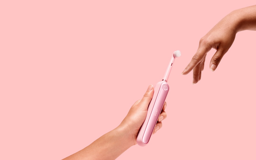 Person holding a pink electric toothbrush to prevent tartar on teeth
