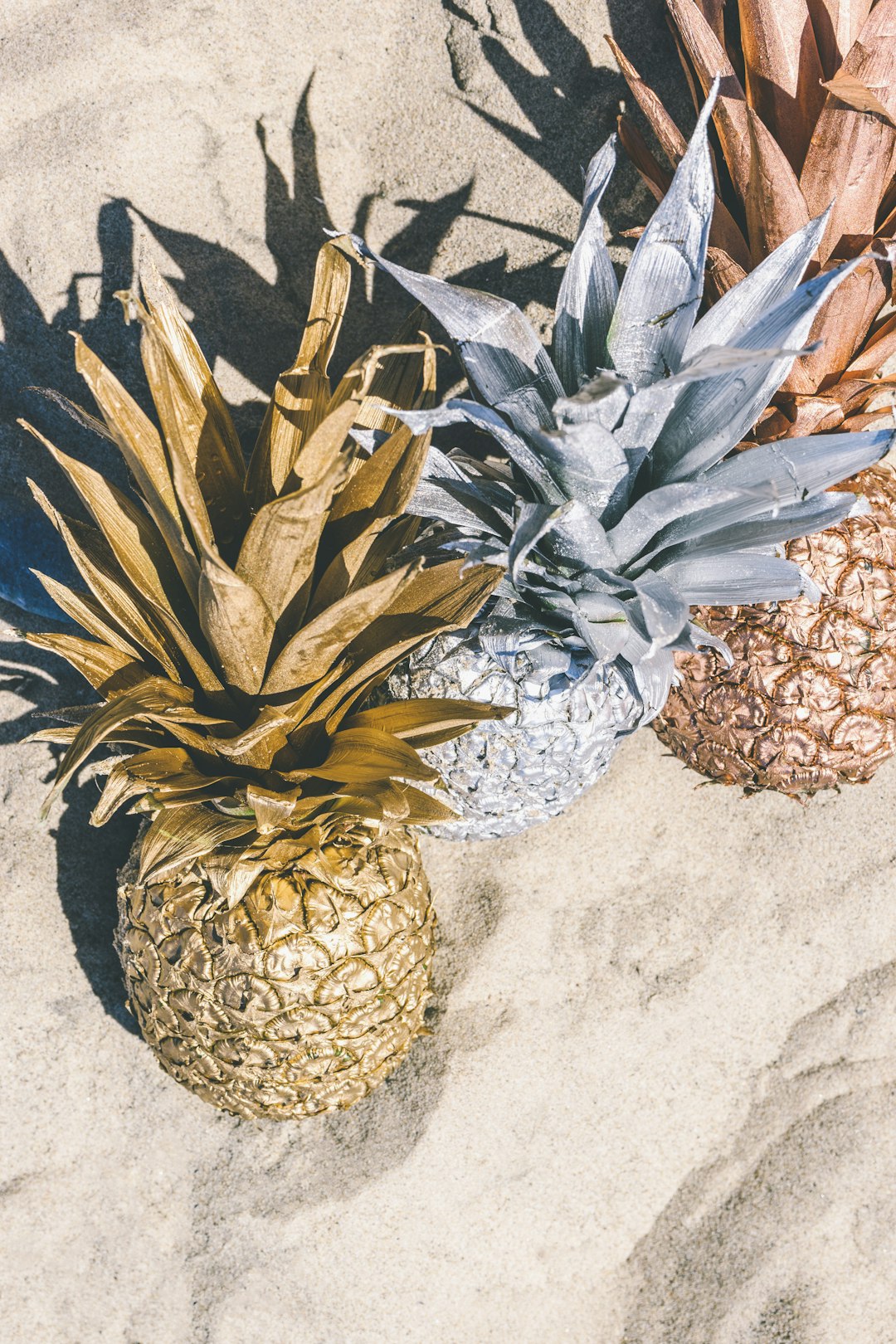 gold, silver, bronze pineapple in sand