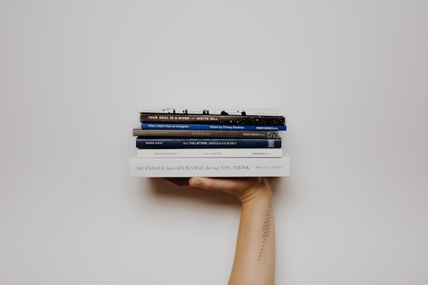 Woman with a tattoo holding up a stack of books. By unsplash user @thoughtcatalog