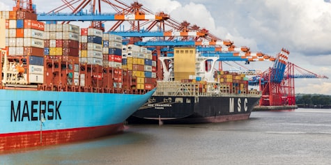 Three large container ships with black hulls and MSC painted on the side tied up at a large wharf with cranes.