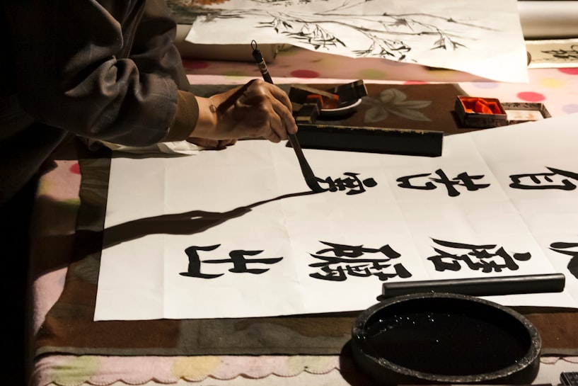 A person's hand writing Chinese calligraphy on a large sheet of paper.